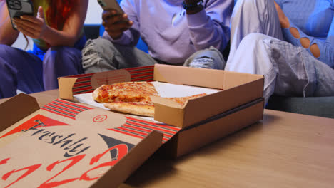 Close-Up-Of-Gen-Z-Friends-Sitting-On-Sofa-Eating-Home-Delivery-Takeaway-Pizza-And-Using-Mobile-Phones